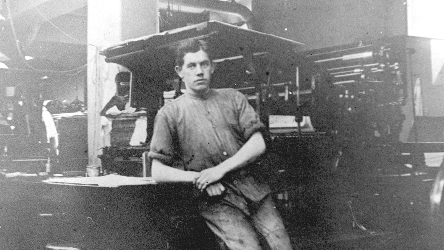 An old black and white photograph showing a young man in rolled-up shirt sleeves leaning on a machine.