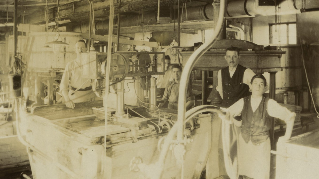 A black and white picture of people working at the mill, standing around a machine. 
