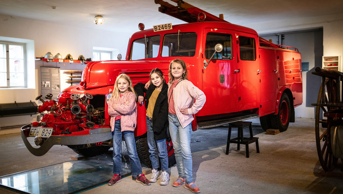 Three children standing in front of a fire truck in the museum's firehouse