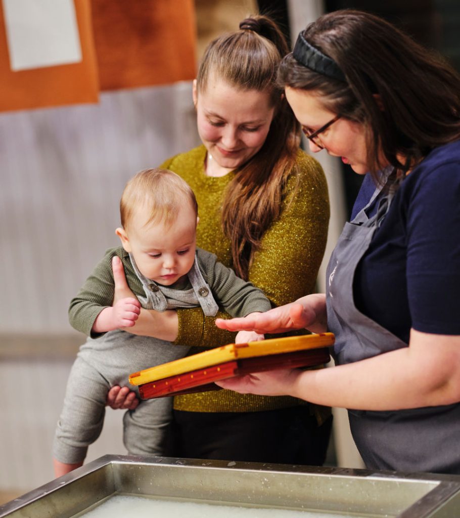 Förälder och bebis gör papper tillsammans med en museipedagog. 