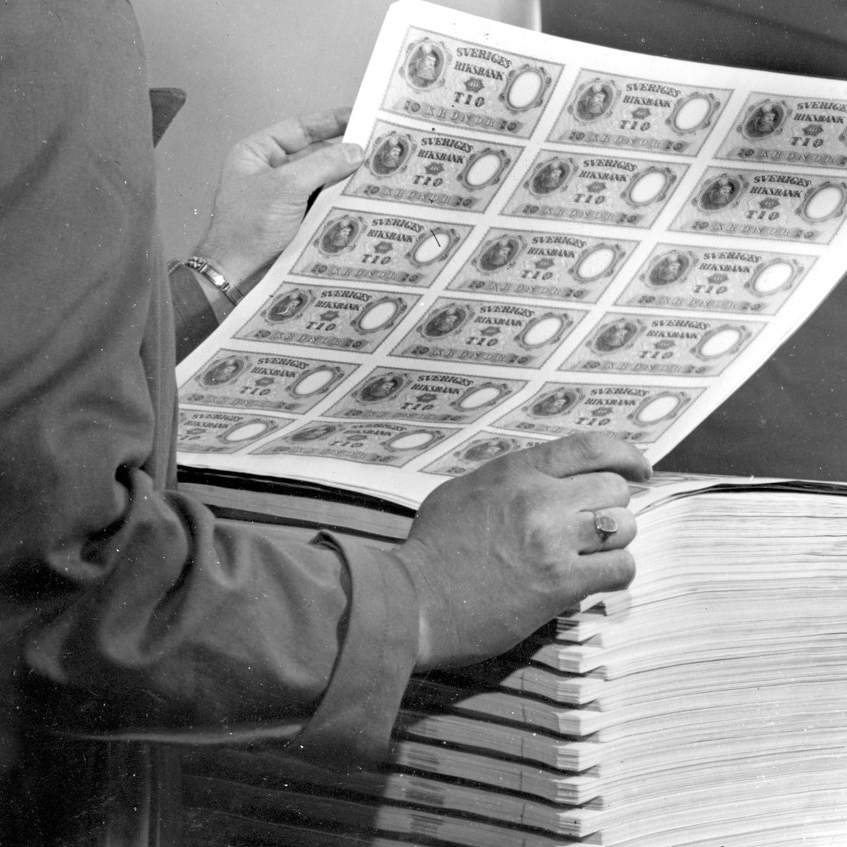 Svartvit bild av en man som håller i ett ark med  tiokronorssedlar från 1940. 
