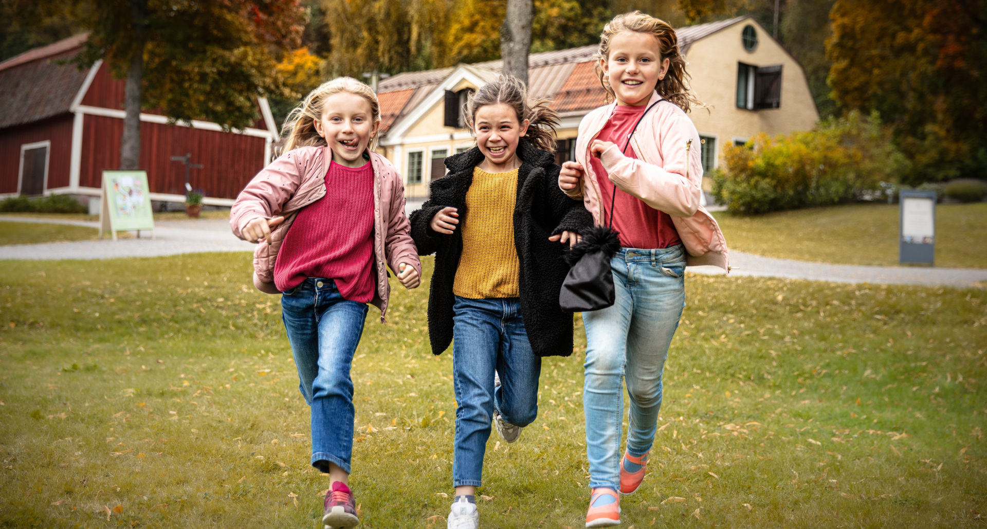 Three children run and laugh in a park.