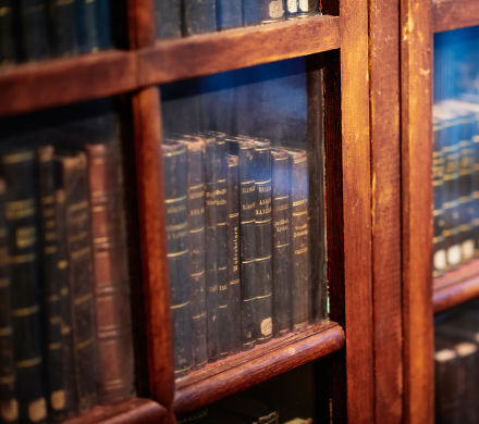Närbild på antika böcker bakom en inglasad bokhylla