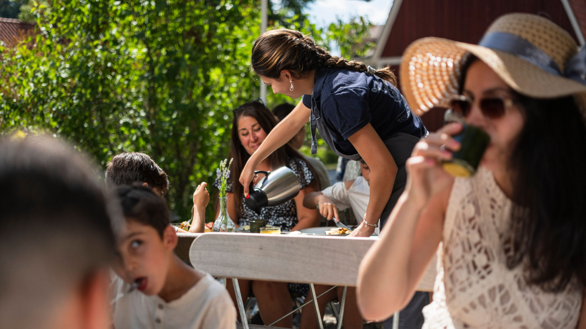 Adults and children eating and drinking coffee in an outdoor café under trees and parasols