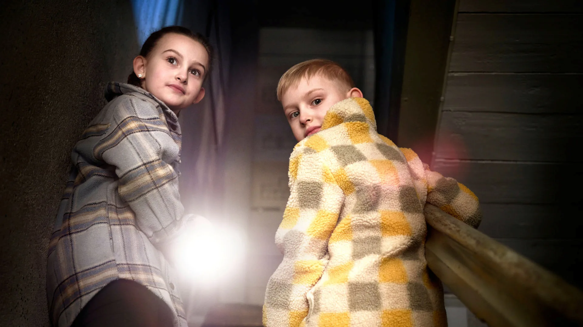 Bild på två barn i en mörk trappa, en av dem håller i en ficklampa.