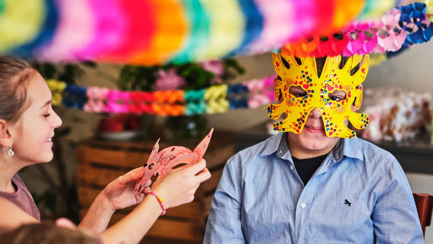 barn med en dekorerad mask, omgiven av vänner och girlanger